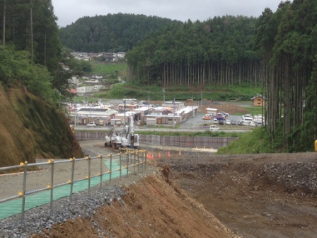 造成中の道路の先に仮設住宅や車が並ぶ市街地が広がり、復興が進む町の様子を高台から見下ろしている、南三陸町の復興風景の写真