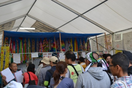 テント内の壁には色とりどりの千羽鶴やメッセージが飾られ、多くのボランティアが集まって説明を受けたり話し合ったりしていている様子を写した写真