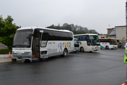 雨の中、ボランティア輸送用と思われる観光バスが3台ほど道路に並んで停車している様子の写真