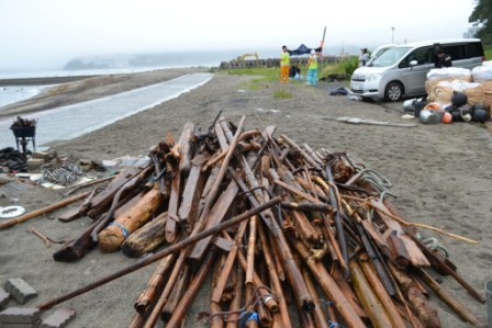 浜辺の砂の上に長さや太さがさまざまな流木が大量にまとめて積み上げられている、流木の集積所の写真