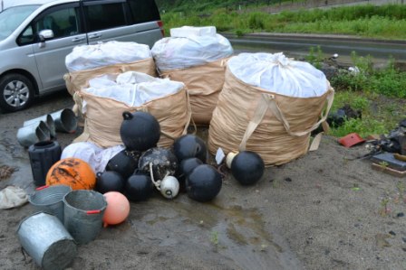 砂浜に並べられた大きな土のう袋に分別されたごみと、黒やオレンジ色の漁業用ブイなどがまとめられている清掃後の分別ごみの写真