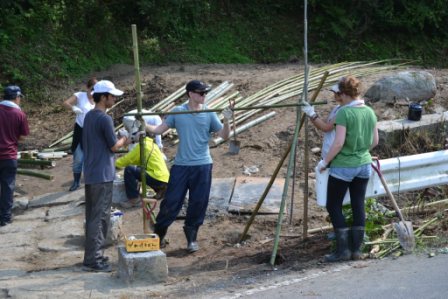 道端で竹を支柱として立てながら、数人の参加者が支え合って骨組みを作っており、基礎の構造づくりに取り組む様子の写真