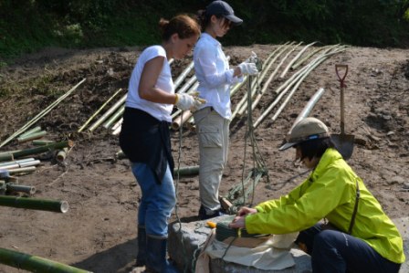 数人の女性が地面に置いた竹を縄で結んだり、細かい作業を行っており、竹を固定するための準備に集中して取り組んでいる様子の写真