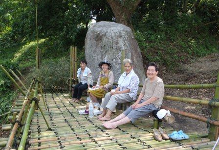 完成した竹のデッキの上で、4人の地元の女性たちが笑顔で腰かけてお茶を楽しんでおり、自然の中でひとときを過ごしている様子の写真