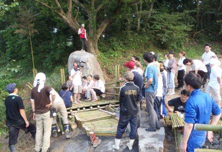 石碑の前に集まったたくさんの人々が、完成した竹のデッキを囲みながら話をしている様子を写した写真