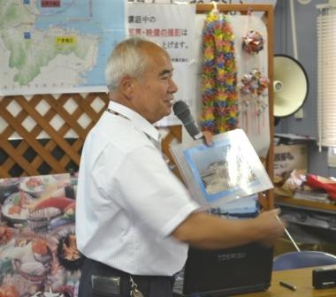 白いシャツを着た後藤一磨さんがマイクを手にしながら話をしている様子の写真