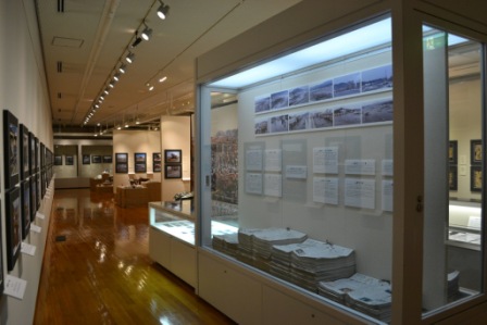 壁一面に震災前後の写真や資料が展示され、ガラスケース内も写真や文書が並び、奥まで展示スペースが続いている様子の写真