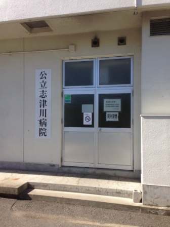 白い外壁の建物の一角に「公立志津川病院」と縦書きで表示され、病院の通用口の写真