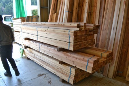 屋内の作業場で、きれいにカットされ青いテープで束ねられた角材が高く積まれて製材された木材の写真