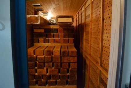 「天井と壁が木で囲まれた乾燥室の中に、丁寧に積み重ねられた角材が隙間なく並べられており、奥には照明の光が差し込んでいる木材乾燥室の写真