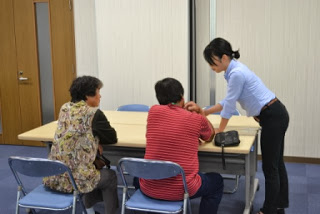 女性スタッフがテーブル越しに座っている二人の高齢女性に向かって指さしながら説明している相談場面の写真