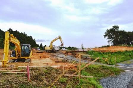 曇り空の下、周囲に緑が広がる空き地の小高い場所に2台のショベルカーが作業している写真