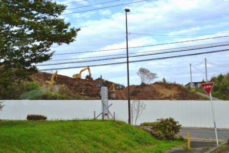 現場全体は白い塀で囲まれており、山のように盛り上がった土の上に複数の重機が作業をしている写真