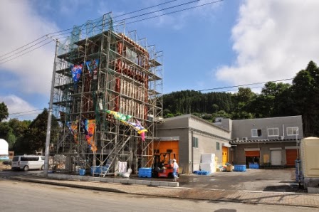 足場が組まれた水産加工場の建物にカラフルな大漁旗が掲げられている建設中の様子を写した写真