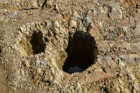 硬い岩盤に円形や楕円形に深く掘られた複数の柱穴跡が確認できる遺跡の柱穴の拡大写真