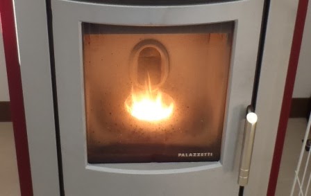 ペレットストーブのガラス扉越しに、内部で木質ペレットが炎を上げて燃えており、周囲がオレンジ色に照らされている写真