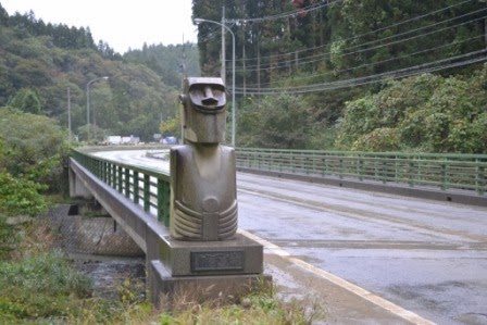 緑色の欄干の橋のたもとに、笑ったような表情のモアイ像が設置されている舘下橋のモアイの写真