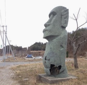 腹部が大きく破損し、中の骨組みが露出した状態となったモアイ像が立っている写真