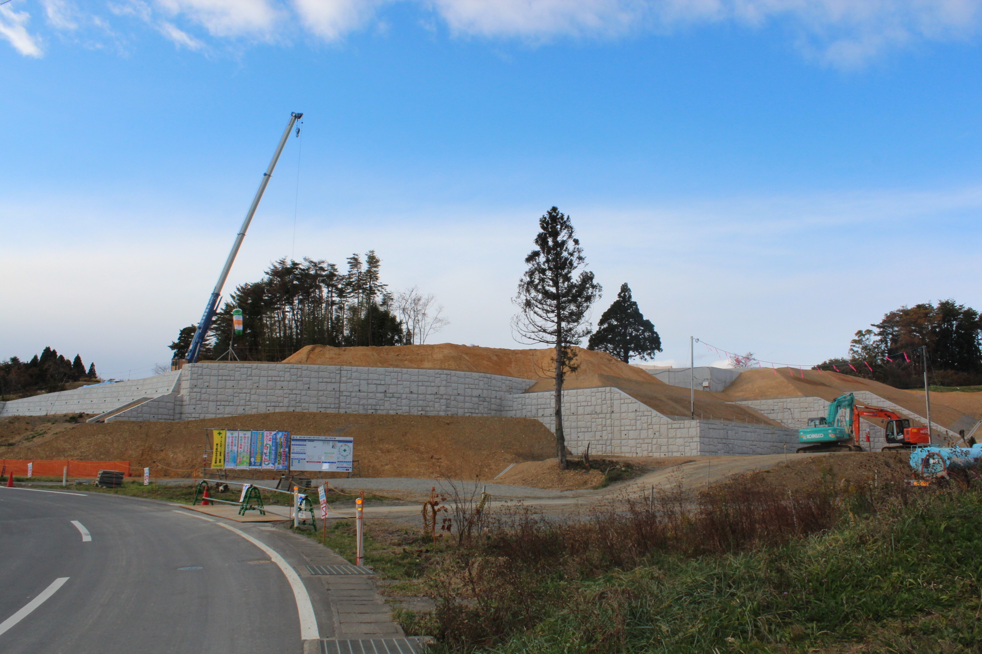山を切り開いて白い擁壁で段差を作った広大な造成地で、クレーン車と重機が配置されている開発初期の写真