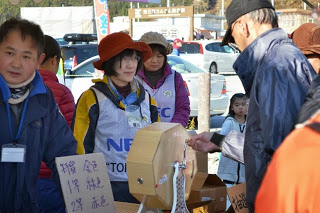屋外の抽選ブースで、来場者の男性がガラガラ抽選機を回している様子を写した写真