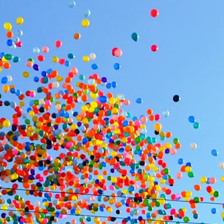 青空の下、無数の色とりどりの風船が空高く舞い上がっている様子を写した写真