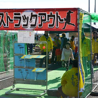 「ストラックアウト」と書かれたコーナーで、子どもが的に向かってボールを投げ、黄色いジャンパーを着たスタッフが見守っている様子を写した写真