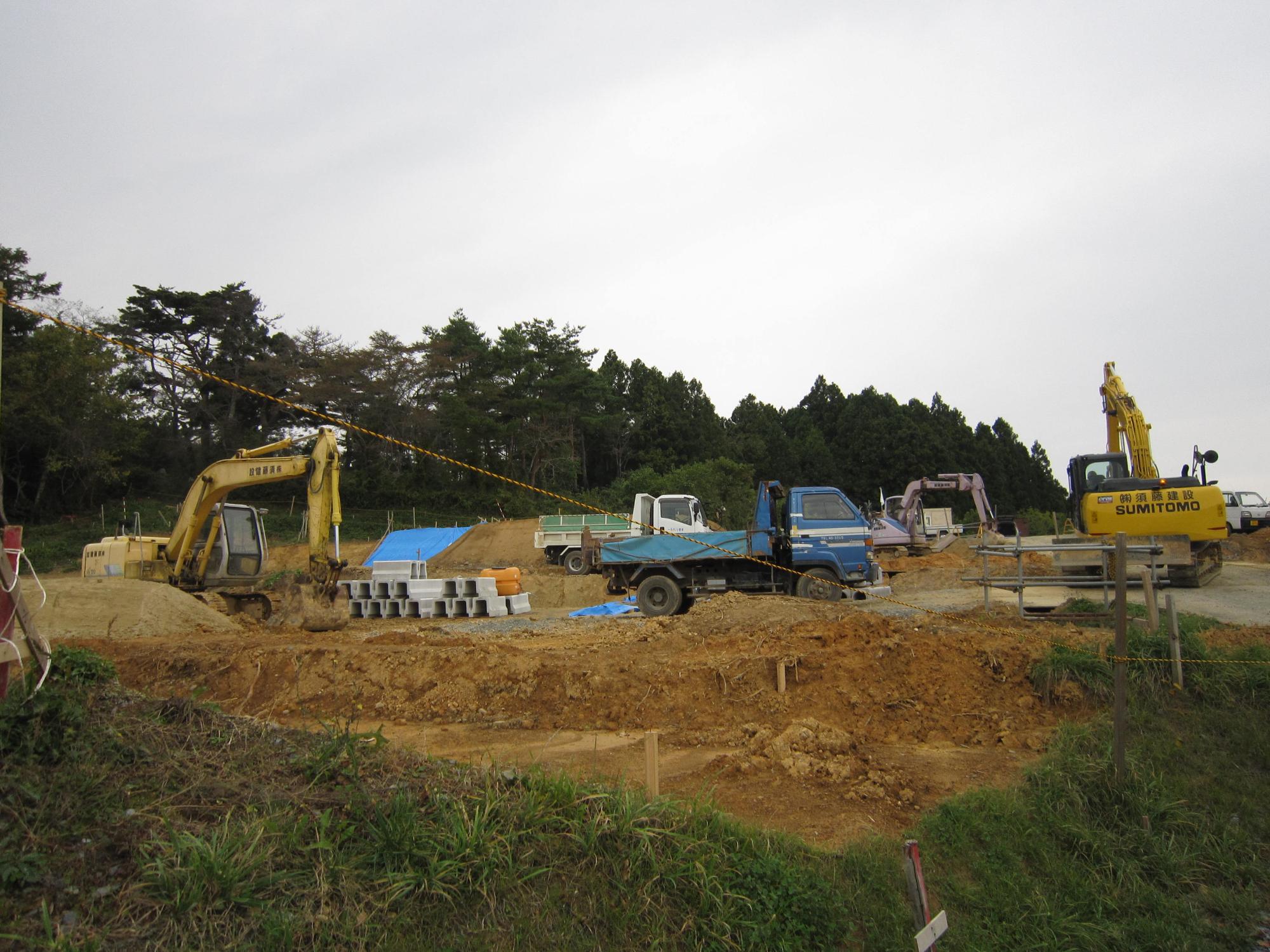 木々に囲まれた土地で、複数のショベルカーやトラックが作業中の造成工事現場の写真