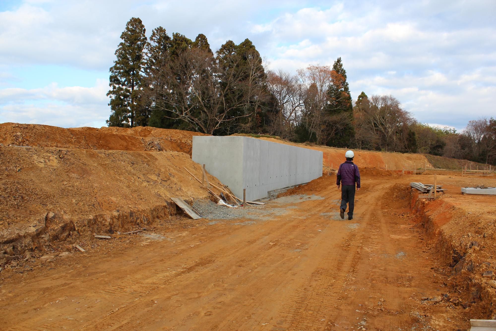 土がむき出しの造成地で、コンクリートの壁の横をヘルメットをかぶった作業員が歩いている造成工事中の写真