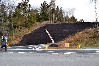 法面に黒い有機素材のマットがしっかりと被せられており、道路は舗装道路が通っている写真