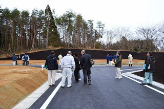 舗装が完了した整備が行われた団地用地で、多くの関係者の方々がアスファルトの道路を歩きながら整備状況を確認している様子の写真