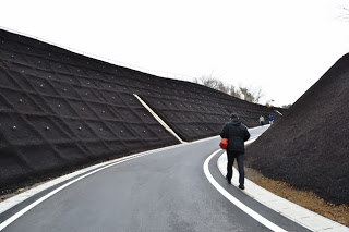 法面に黒い有機素材のマットがしっかりと被せられており、その横をカーブした舗装道路が通っている写真