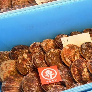 青いコンテナにホタテ貝がぎっしりと並べられており、その上に「専」マークの赤いセリ札と手書きの札が置かれていて、すでに買い手が決まっていることが示されているホタテの写真