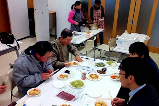 室内で数人の大人たちがテーブルを囲み、トウキリーフを使った料理を試食している様子の写真