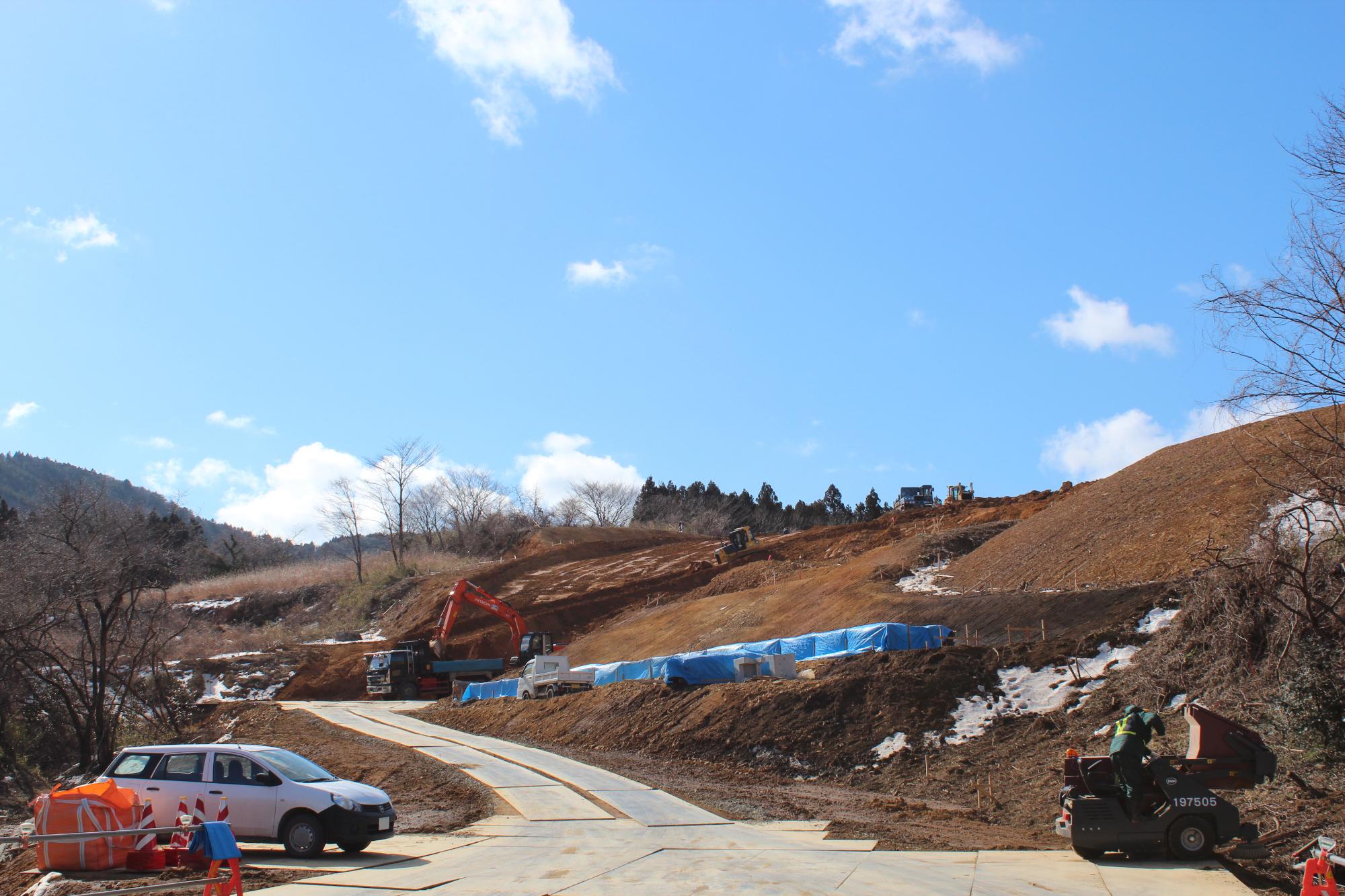 山あいの斜面で複数の重機や作業員が造成工事を行っている様子を写した写真
