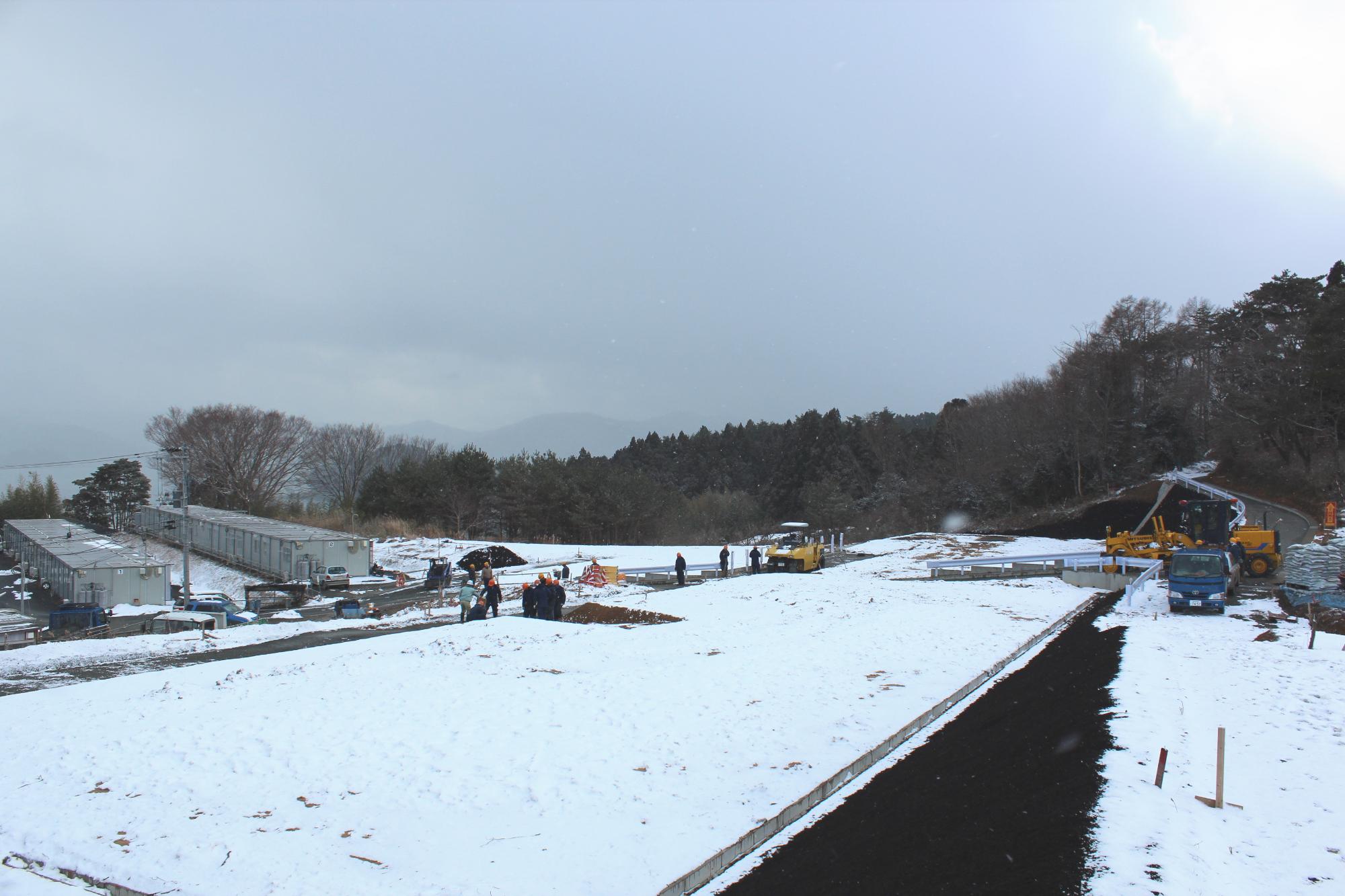 一面が雪景色の中で、作業員たちが造成工事を進めている冬の開発現場の写真