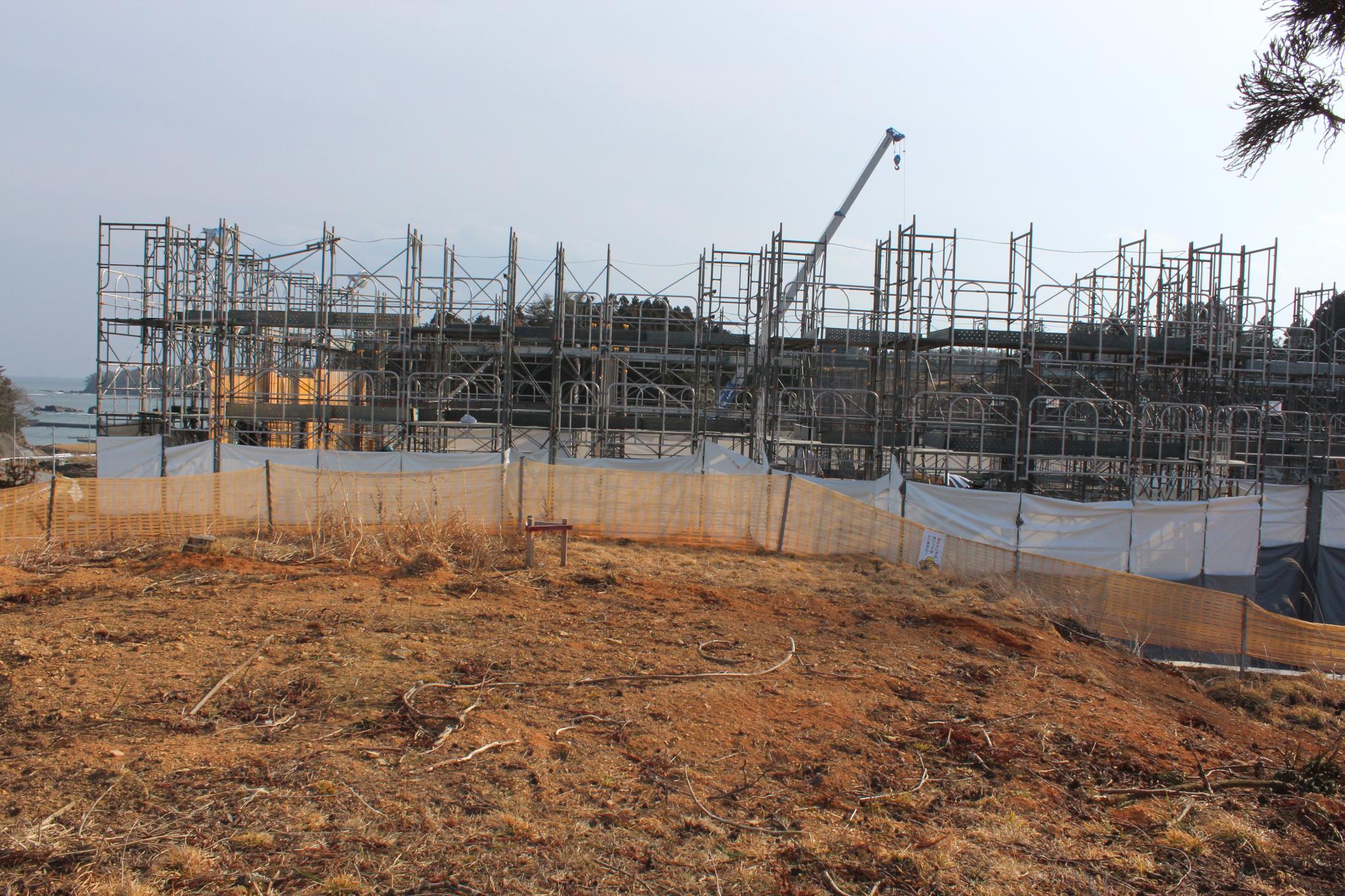 遠くに海が見える高台で、鉄骨の骨組みが組まれている建設中の建物の写真