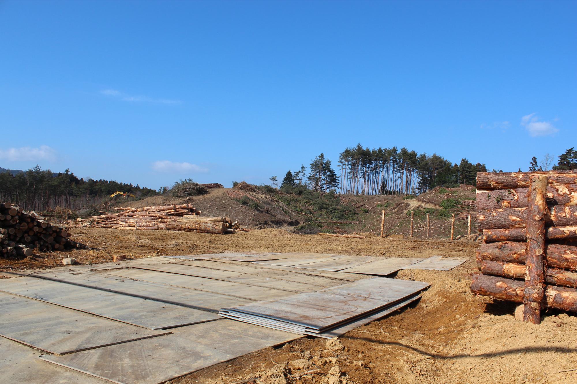 木を伐採した後の斜面に木材が積まれ、仮設の鉄板が敷かれた造成地の写真
