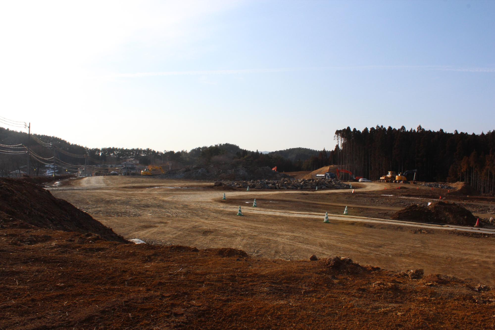 広大な造成地に複数の重機が点在し、岩を砕いたり地面をならしたりしている最中の開発途中の写真