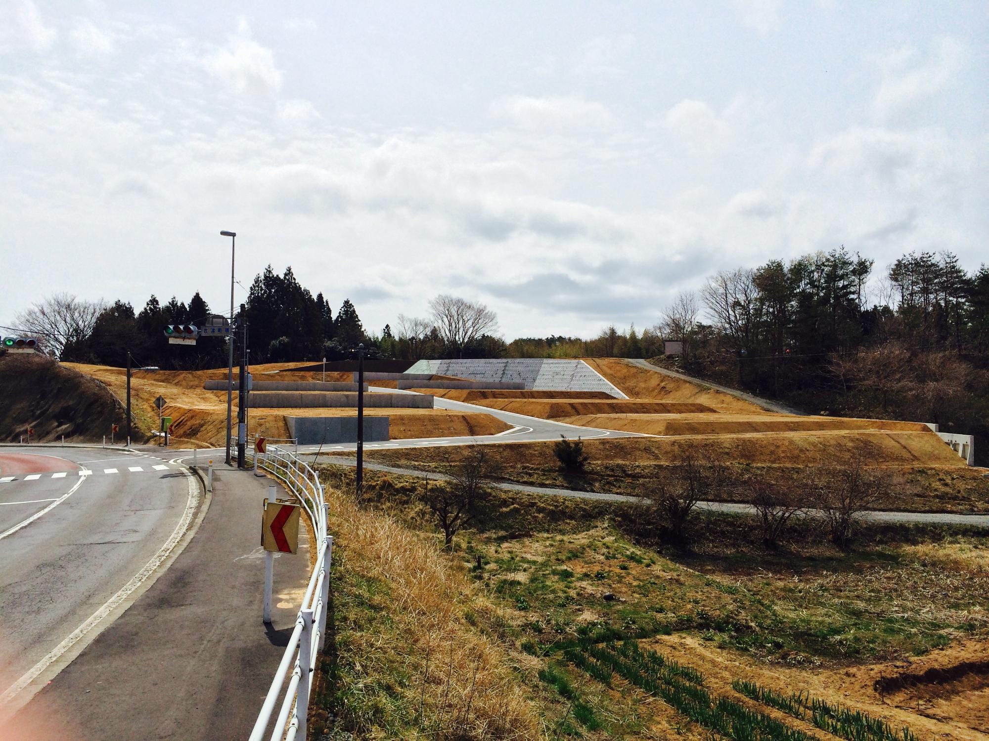 坂道に沿って階段状に区画された整地済みの土地が広がり、舗装道路と信号機が見える造成地の完成直前の写真