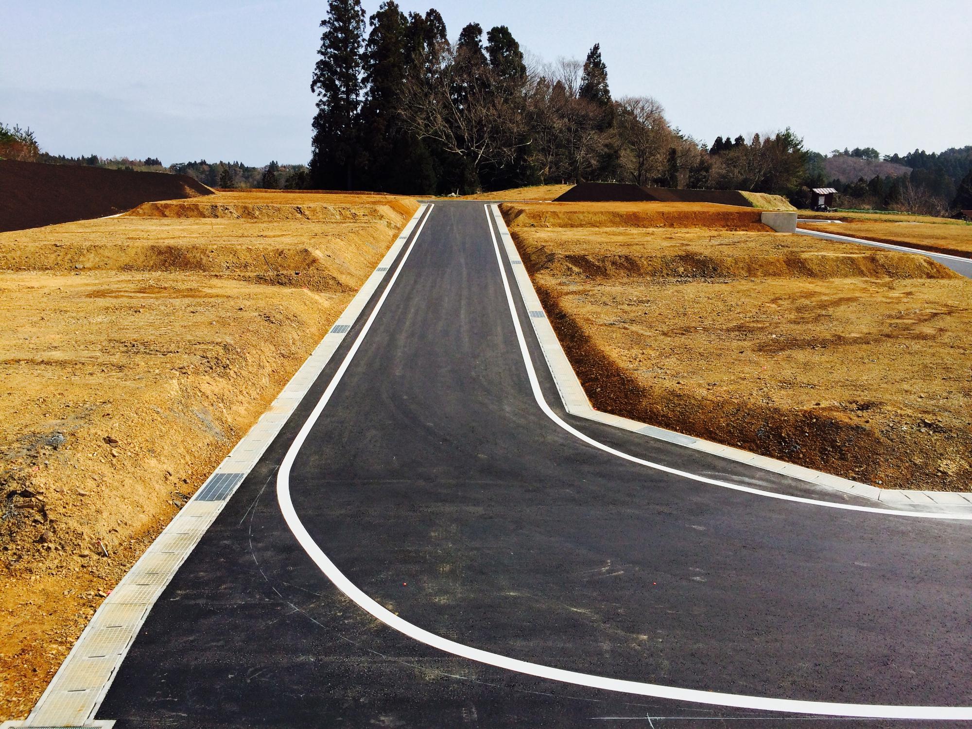 L字型にカーブした新しく舗装された道路の両側に整地された土地が広がっている新興住宅地の写真