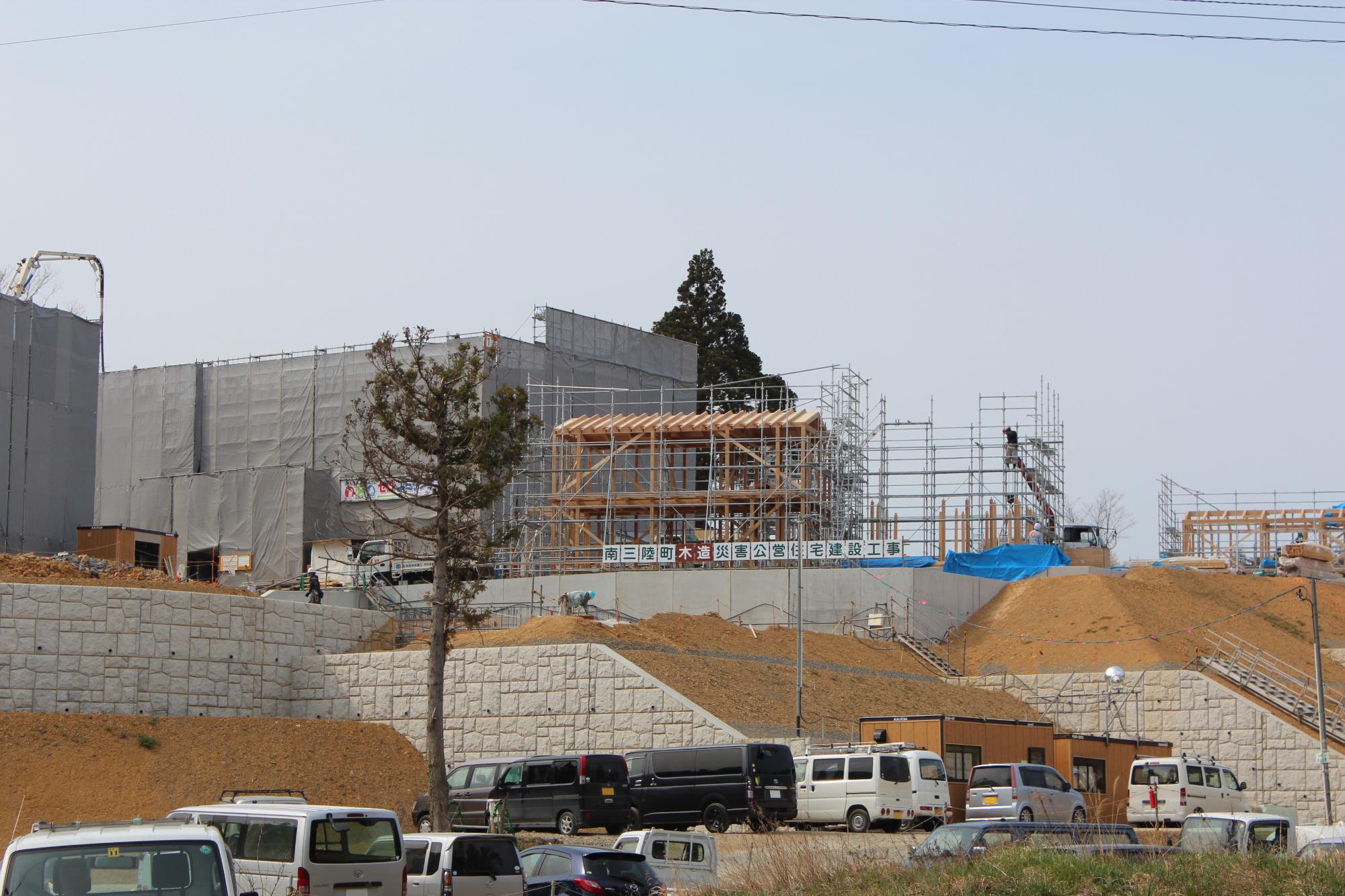 木造の骨組みが立ち上がり、工事関係車両が集まる高台の災害公営住宅の建設現場の写真