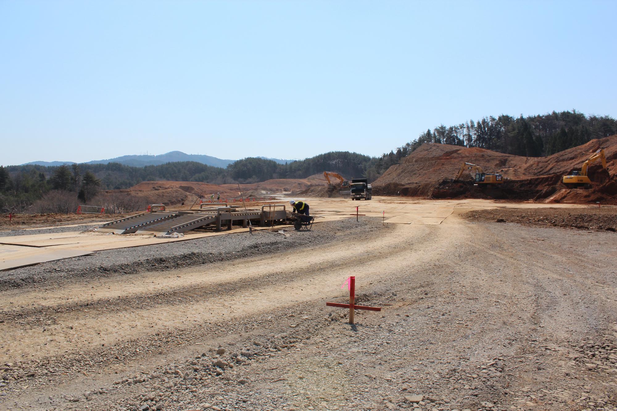 山間の広大な土地で、重機と作業員が地面を整備している写真