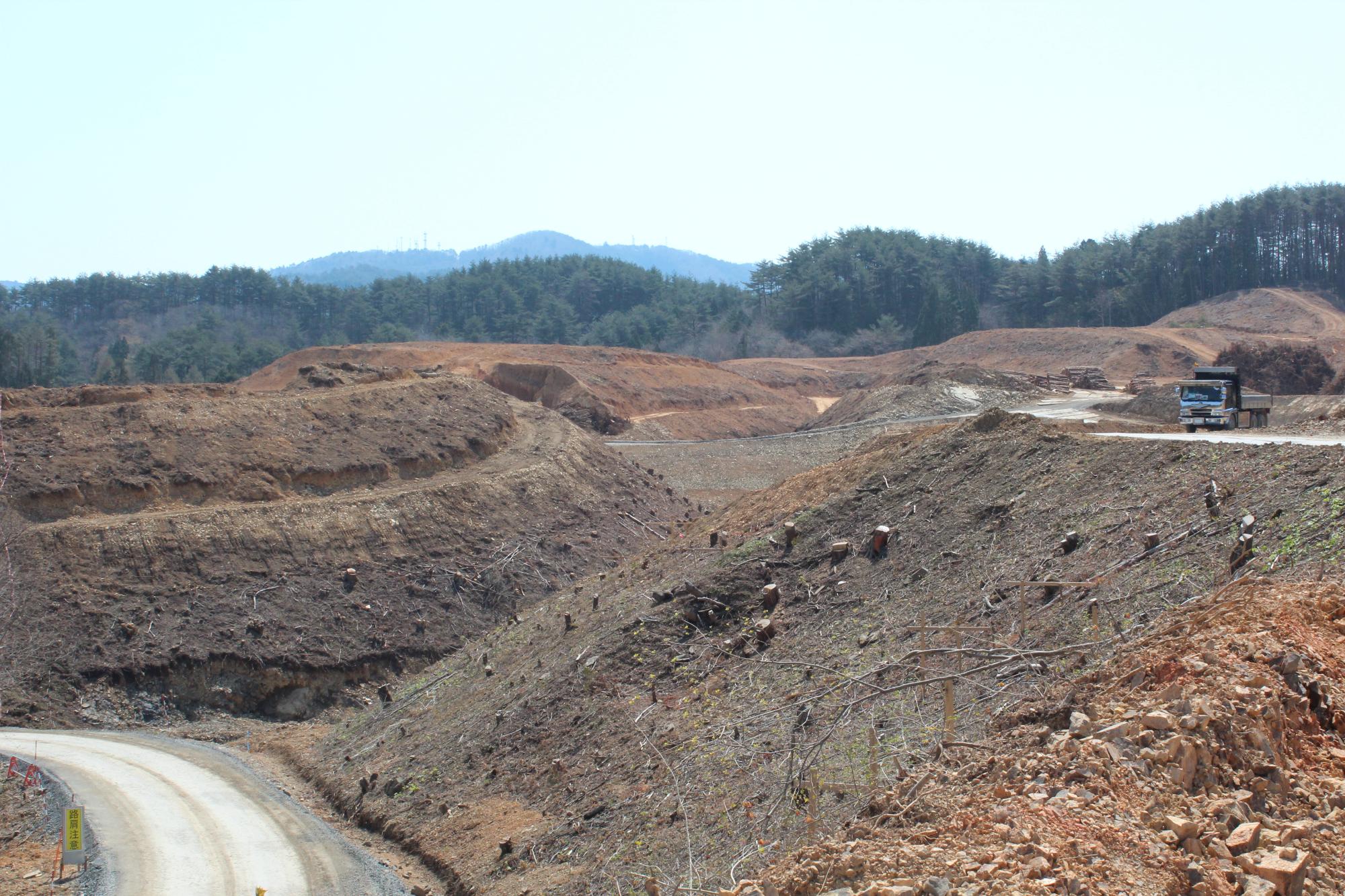 木々が伐採され造成中の山の平らになった場所をダンプトラックが走っている写真