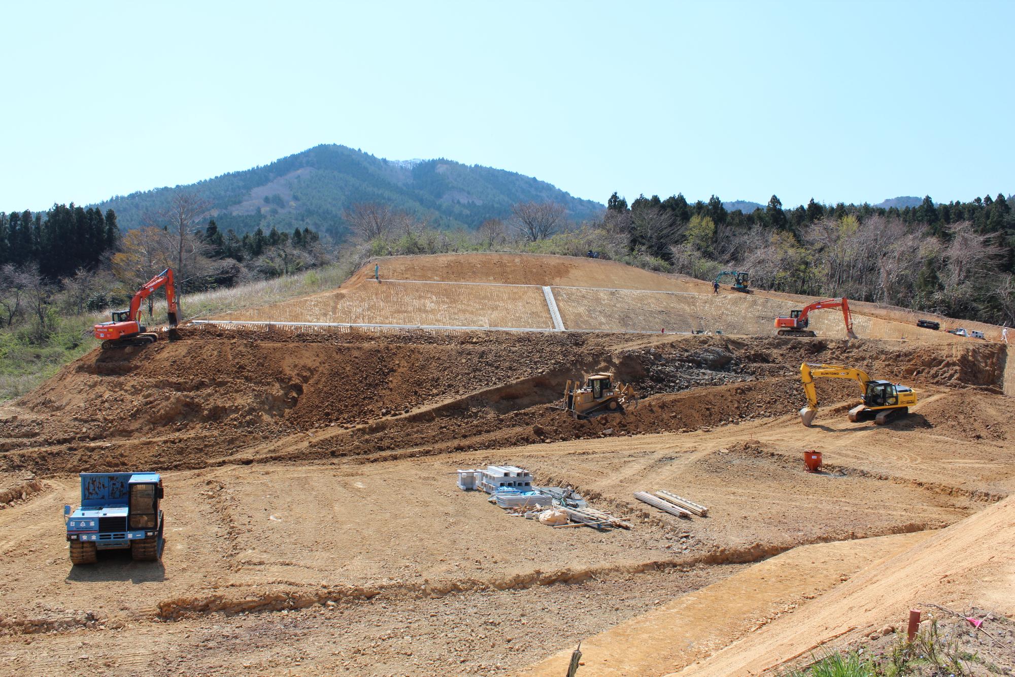 山の斜面で重機が土をならしながら造成工事を進めている様子を写した写真