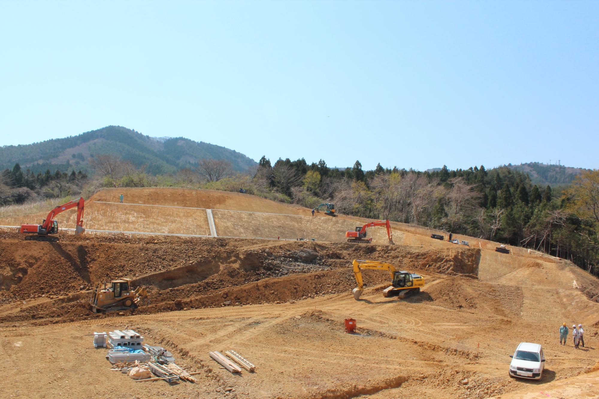 山の斜面で複数の重機が整地作業を進め、作業員と車両が配置された造成地の様子を写した写真