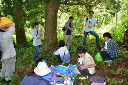 森の中で青いレジャーシートを囲みながら、木陰で休んだり立ち話をしている参加者の写真