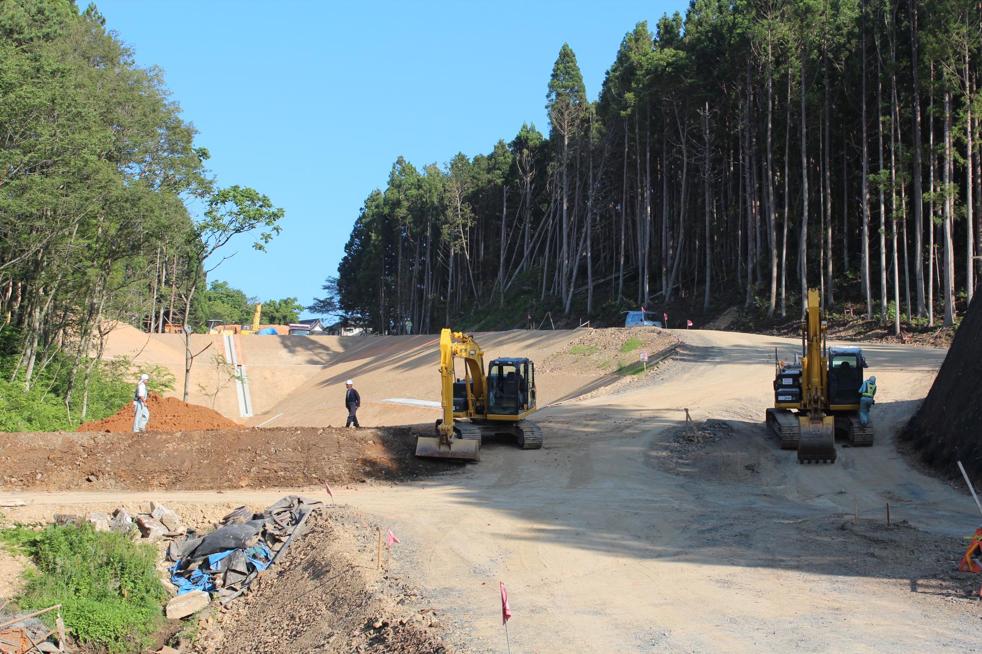 中央に2台のショベルカーがあり、両側に傾斜がある造成現場で工事作業員が歩いている造成作業中の写真