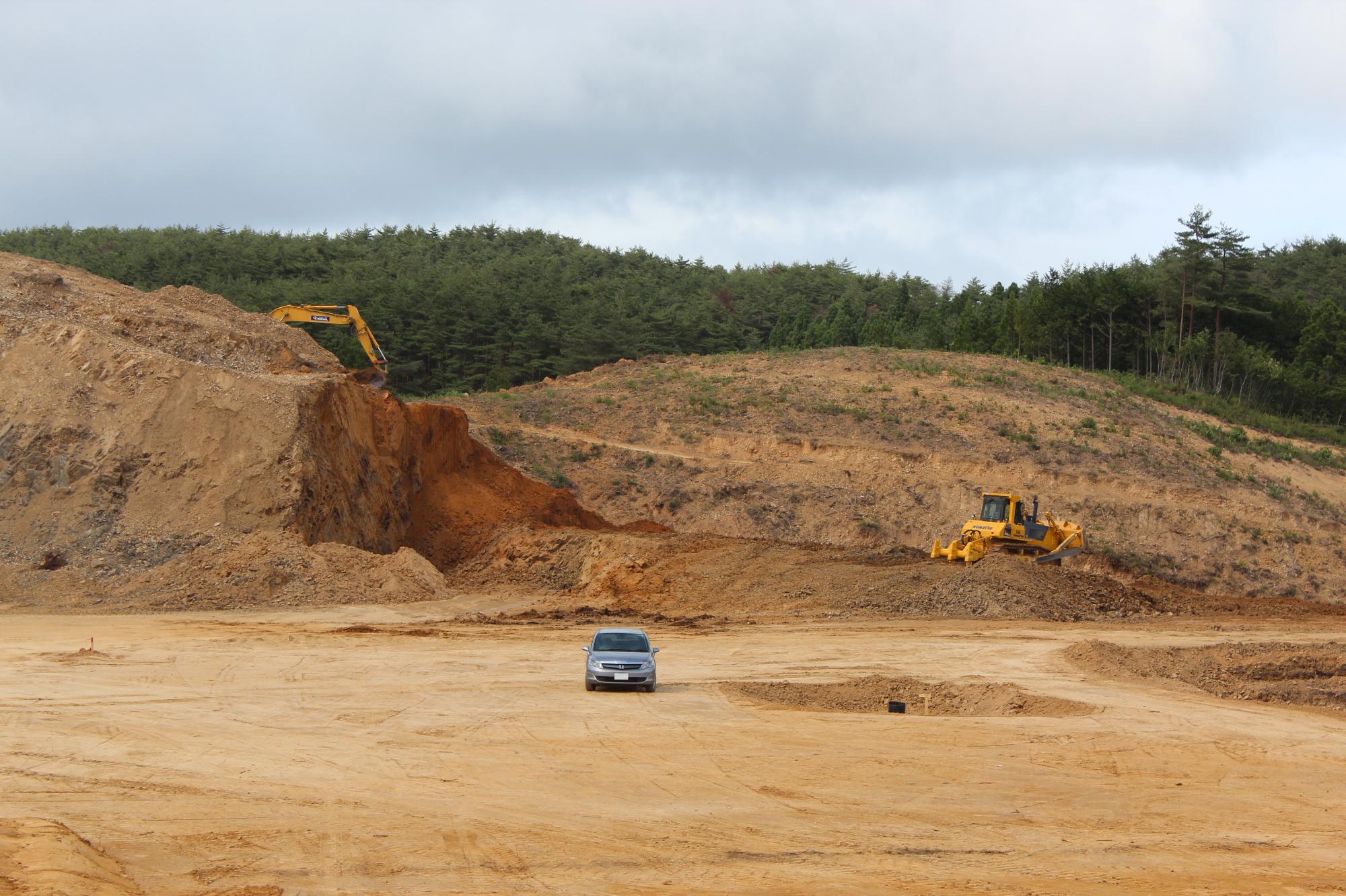 広大な赤土の造成地にブルドーザーとショベルカーが作業している様子の写真