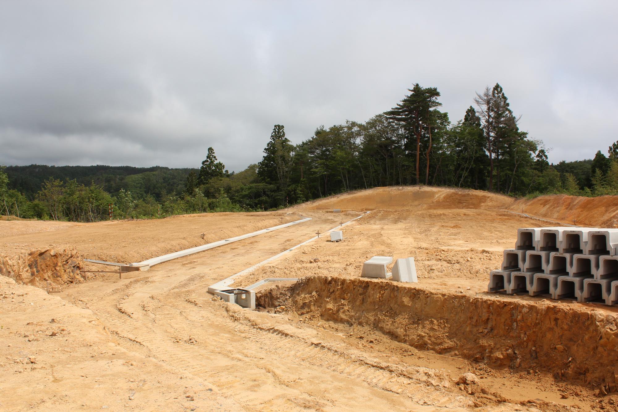 土がむき出しの造成地にU字溝が配置され、コンクリートブロックが積まれている山間の広い敷地の写真