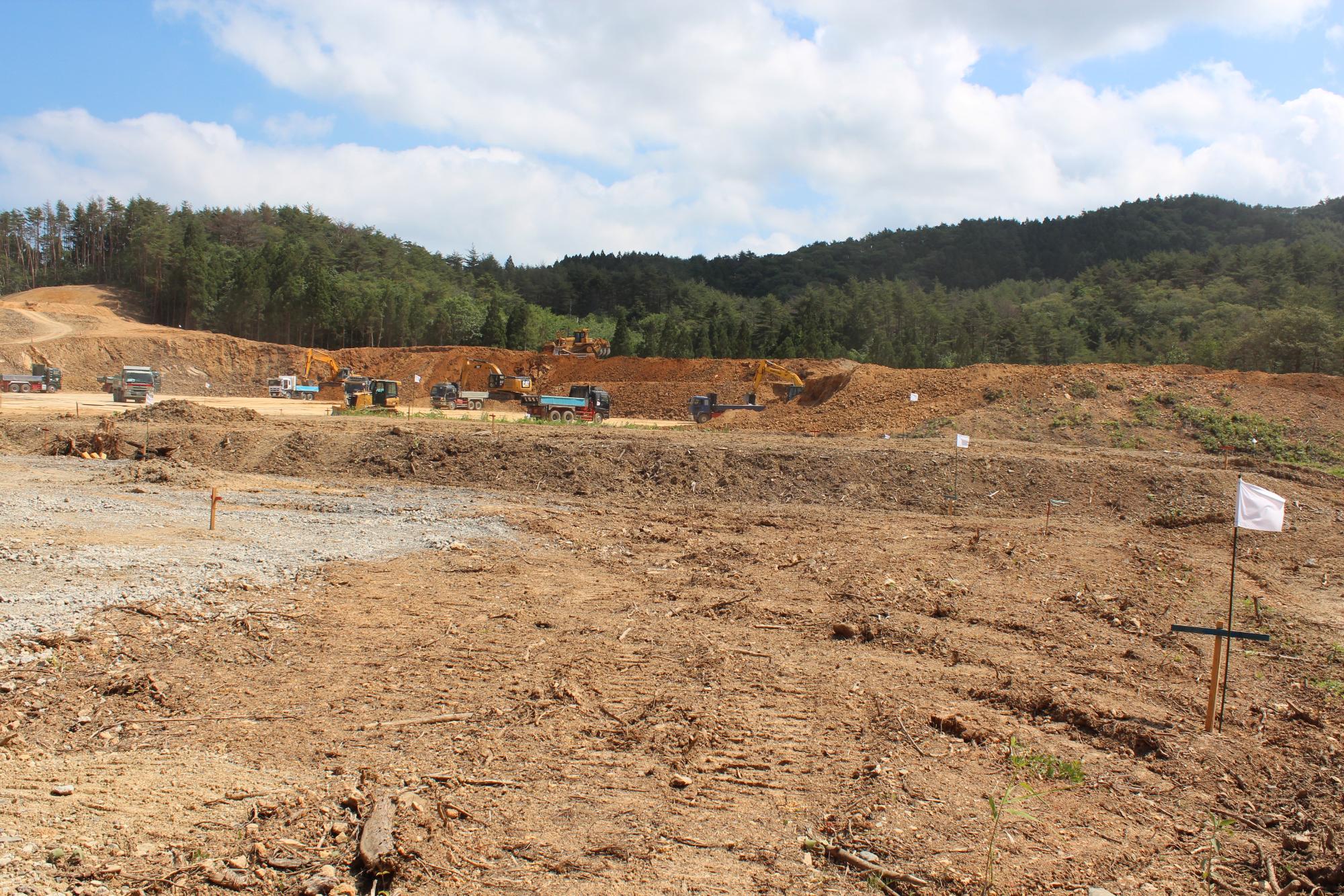 山あいの開けた場所で多数の重機やトラックが土を掘削している様子の写真